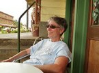 Dr. Louise Mcreynolds, a woman with short, grey hair and a blue shirt sits on a chair on a balcony. She is smiling and wearing sunglasses.